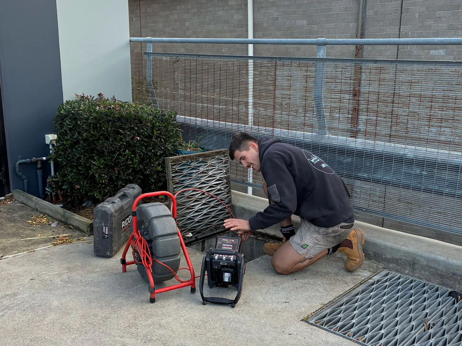 Plumber feeding a drain camera into a pit at a commercial unit